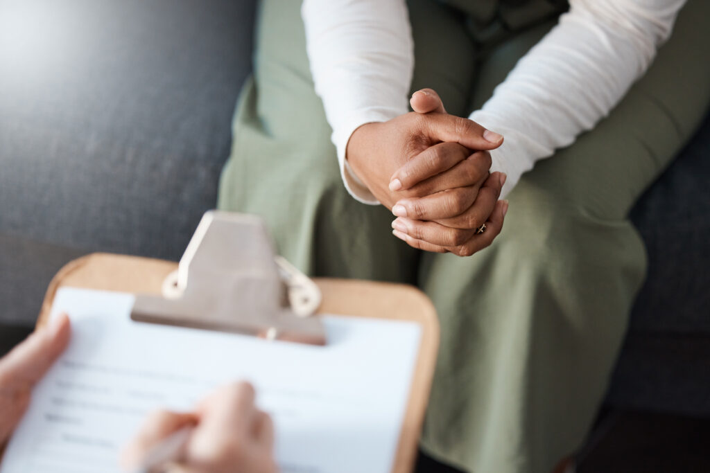 Woman, hands and therapist writing on clipboard in consultation for mental health, psychology or healthcare. Hand of female person or psychologist consulting patient with anxiety or stress in therapy.